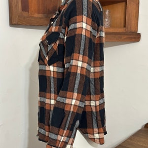 May include: A long-sleeved plaid shirt in black, brown, and white. The shirt has a button-down collar and two chest pockets.