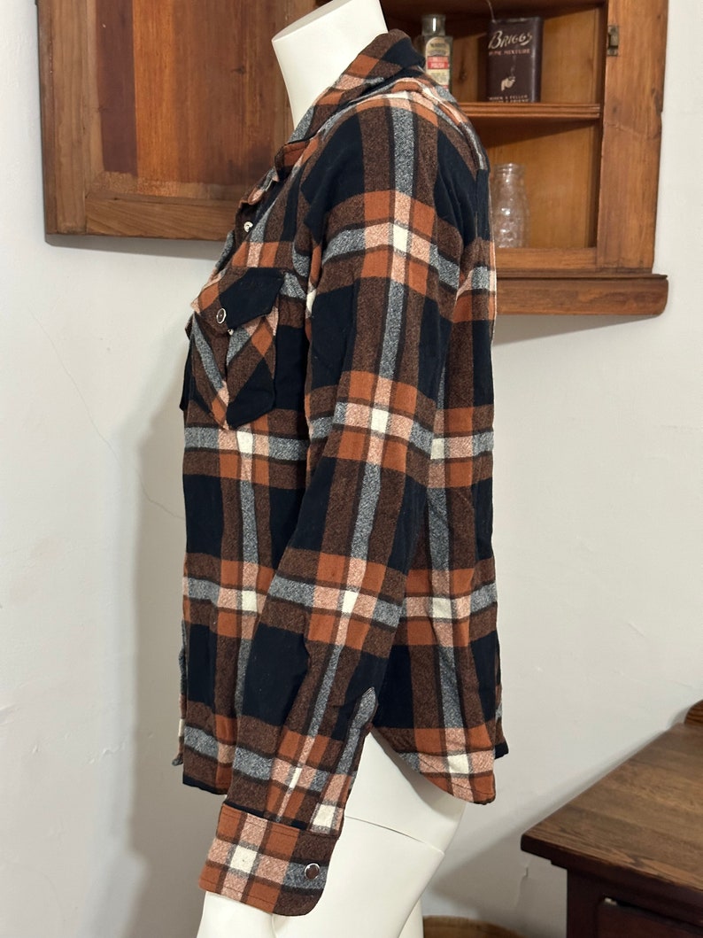 May include: A long-sleeved plaid shirt in black, brown, and white. The shirt has a button-down collar and two chest pockets.