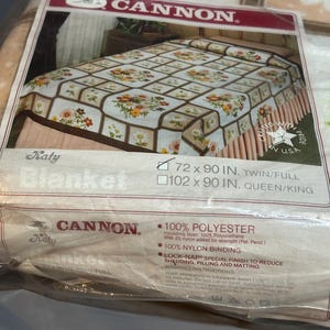 May include: A Cannon Katy blanket in its original packaging. The blanket features a floral pattern in a grid design with brown and beige tones. The packaging indicates the blanket is 72 x 90 inches, suitable for a twin or full bed.