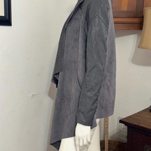 Pu&ograve; includere: Giacca grigia drappeggiata con maniche in ecopelle. La giacca ha un davanti a cascata e una vestibilit&agrave; morbida. Le maniche sono di un grigio pi&ugrave; scuro rispetto al corpo. La giacca &egrave; esposta su un manichino.
