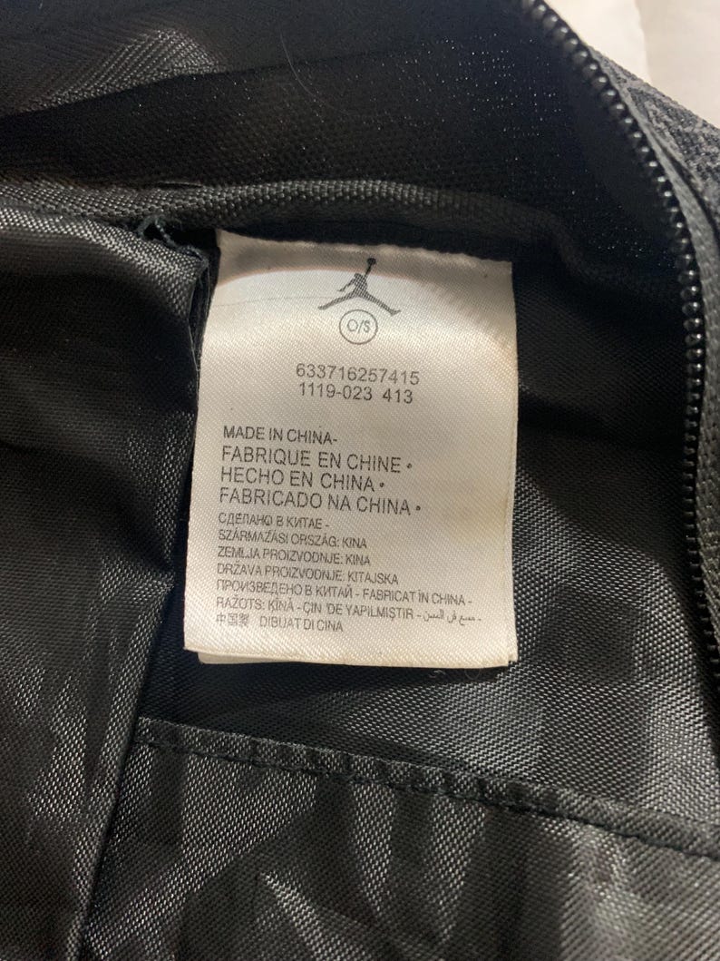 K&ouml;nnte beinhalten: Ein wei&szlig;es Etikett mit schwarzem Text auf schwarzem Hintergrund. Das Etikett lautet "Made in China - Fabrique en Chine - Hecho en China - Fabricado na China" und enth&auml;lt eine Liste von L&auml;ndern und Sprachen mit dem Text "Made in China".