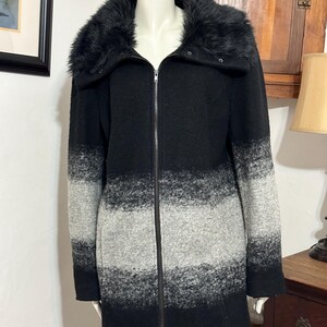 May include: Black and gray striped long-sleeved coat with a black faux fur collar. The coat has a zipper closure and a button at the neck.