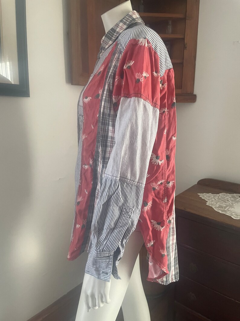 Pode incluir: Uma camisa de bot&otilde;es de manga comprida com um design de patchwork. A camisa &eacute; feita de diferentes tecidos, incluindo xadrez, listras e padr&otilde;es florais. A camisa &eacute; vermelha, azul e branca.