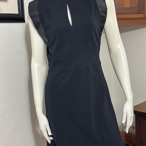 May include: A black sleeveless dress with a keyhole neckline and black leather trim on the straps.