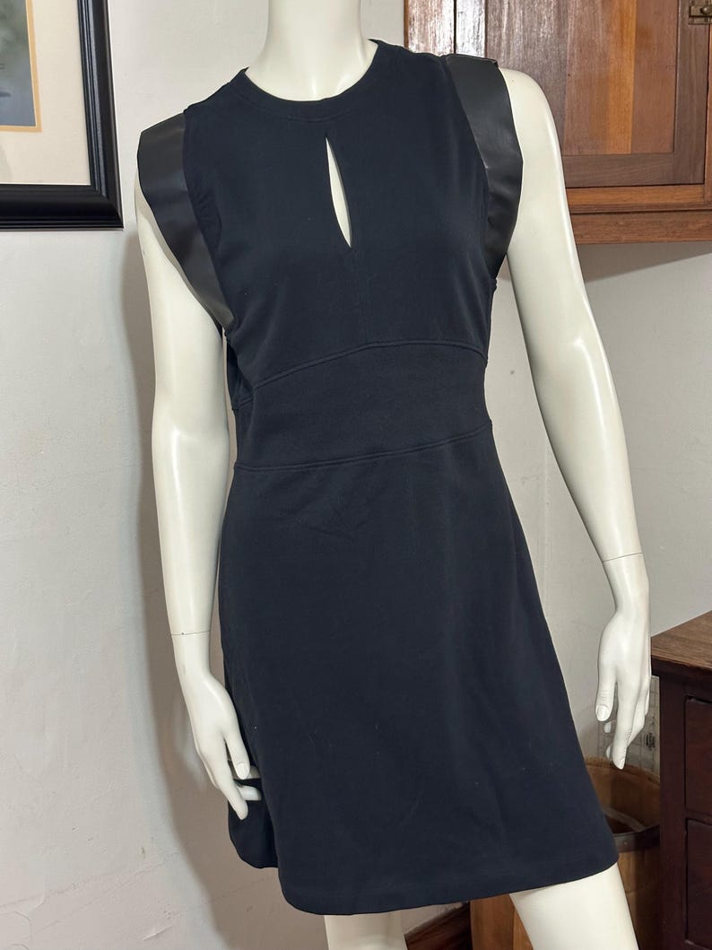 May include: A black sleeveless dress with a keyhole neckline and black leather trim on the straps.