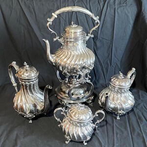 May include: A silver tea set with a teapot, creamer, sugar bowl, and a coffee pot. The set has a decorative, ornate design with a fluted pattern.