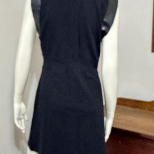 May include: A black sleeveless dress with faux leather trim on the shoulders. The dress has a fitted bodice and a slightly flared skirt.