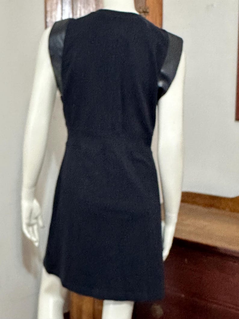 May include: A black sleeveless dress with faux leather trim on the shoulders. The dress has a fitted bodice and a slightly flared skirt.
