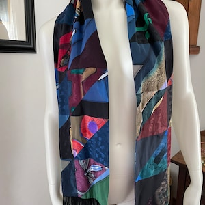 May include: A colorful silk scarf with a geometric pattern in shades of blue, green, red, and black. The scarf has a fringe border.
