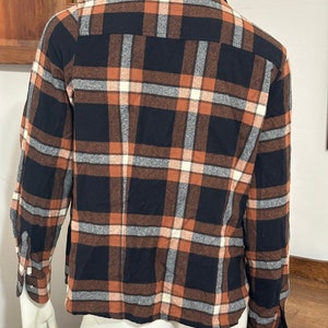 May include: A long-sleeved plaid shirt with a black, brown, and white checkered pattern. The shirt has a button-down collar and long sleeves with button cuffs.