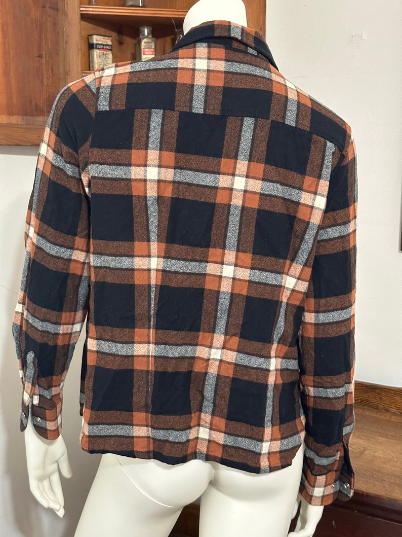 May include: A long-sleeved plaid shirt with a black, brown, and white checkered pattern. The shirt has a button-down collar and long sleeves with button cuffs.
