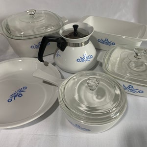May include: A set of white ceramic cookware with blue floral designs. The set includes a casserole dish, a teapot, a baking dish, and two covered dishes.