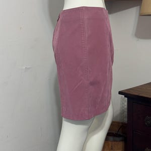 Op de afbeelding: Een stofroze minirok op een mannequin. De rok heeft verticale naden en een knoopsluiting. De stof lijkt op zacht su&egrave;de. De rok wordt van opzij getoond.