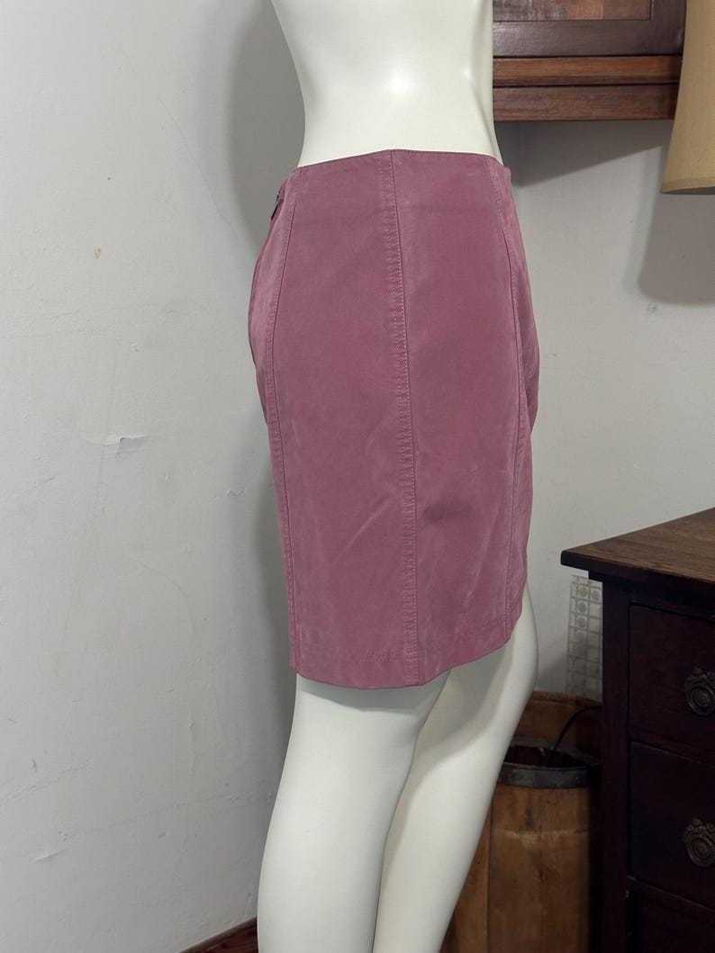 Op de afbeelding: Een stofroze minirok op een mannequin. De rok heeft verticale naden en een knoopsluiting. De stof lijkt op zacht su&egrave;de. De rok wordt van opzij getoond.