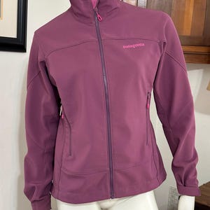 May include: A purple Patagonia fleece jacket with a zipper closure and a pink logo.