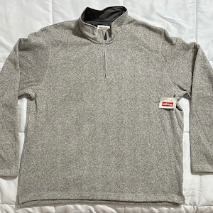 May include: A gray Wrangler fleece pullover with a quarter-zip closure and a mock neck collar. The long-sleeved shirt has a textured appearance and a small tag attached near the bottom. The fleece is a neutral color.