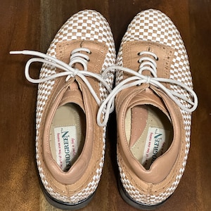 May include: A pair of tan and white checkered leather shoes with white laces. The shoes have a black rubber sole and the text "The art of fine shoe making EROGREEN Styled in Italy" is printed on the inside of the shoes.
