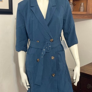 May include: A blue blazer dress with a double breasted closure, a belt, and two pockets. The dress has a v-neck and 3/4 sleeves.