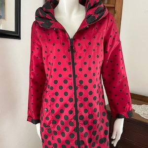 May include: A red and black polka dot raincoat with a black zipper and a black hood. The hood has a black and white floral print lining.
