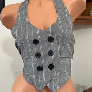 May include: A gray and white striped halter top with a double-breasted button closure. The top has a pointed hem and is made of a lightweight fabric.