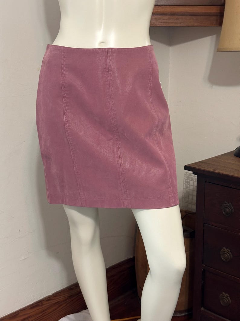 Op de afbeelding: Een stoffen mini-rok in een roze kleur. De rok is gemaakt van een zacht, fluwelig materiaal en heeft verticale naden. De rok wordt op een mannequin gepresenteerd.