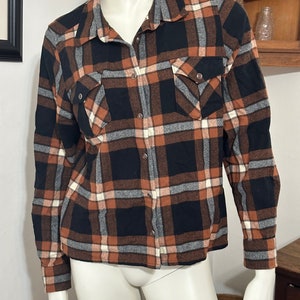 May include: A long-sleeved plaid shirt with a brown, black, and white checkered pattern. The shirt has a button-down front and two chest pockets.