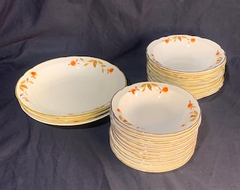 May include: A set of vintage Autumn Leaf dinnerware featuring a stack of 12 white bowls with a gold rim and a stack of 4 white dinner plates with a gold rim. The bowls and plates have a pattern of orange and brown leaves.