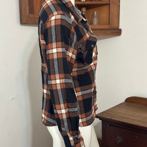 May include: A brown, black, and white plaid flannel shirt with long sleeves and a button-down collar.