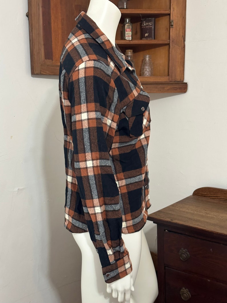 May include: A brown, black, and white plaid flannel shirt with long sleeves and a button-down collar.