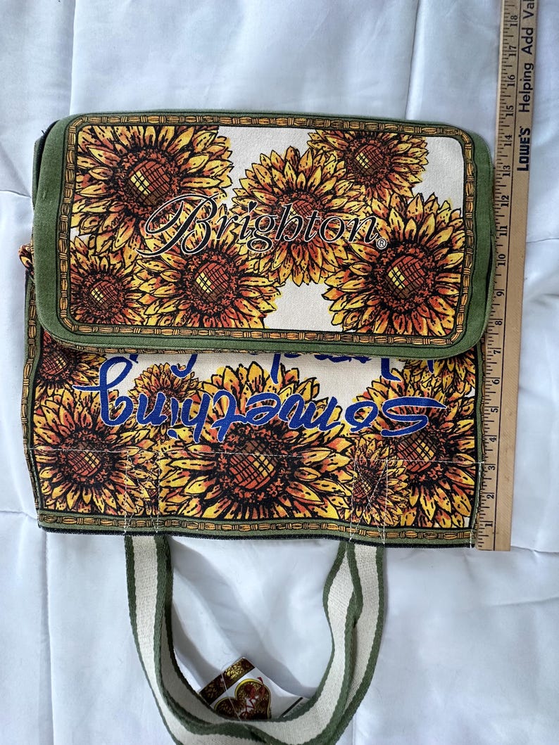 Peut inclure: Un sac fourre-tout rectangulaire avec un rabat, orn&eacute; d'un motif de tournesols sur un fond cr&egrave;me. Le sac a une bordure et des poign&eacute;es vertes. Le mot "Brighton" est imprim&eacute; sur le rabat, et les mots "Something" sont imprim&eacute;s sur le corps du sac.