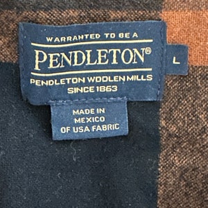 May include: A black and brown plaid Pendleton shirt with a label that reads "WARRANTED TO BE A PENDLETON&reg; PENDLETON WOOLEN MILLS SINCE 1863 MADE IN MEXICO OF USA FABRIC" and a size label that reads "L".