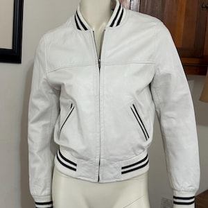 May include: White leather bomber jacket with black and white striped trim around the collar, cuffs, and hem.