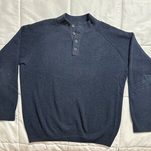 May include: A navy blue ribbed knit sweater with a mock neck and three button closure. The long-sleeved sweater is made of a soft material and is suitable for cooler weather.
