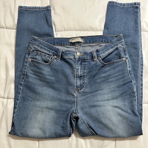 May include: A pair of blue denim jeans with a high waist and a skinny fit. The jeans have a zip fly and button fastening. The jeans are made from a soft, stretchy denim.