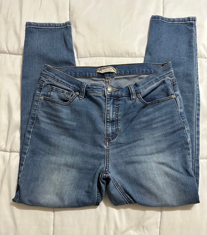 May include: A pair of blue denim jeans with a high waist and a skinny fit. The jeans have a zip fly and button fastening. The jeans are made from a soft, stretchy denim.