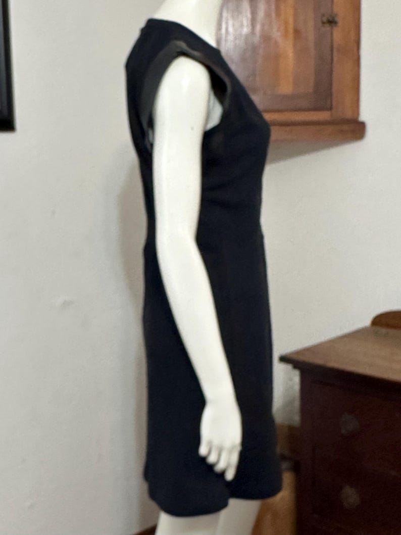 May include: A black sleeveless dress with a leather detail on the shoulders. The dress is fitted and has a straight skirt.
