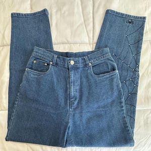 May include: A pair of dark blue denim jeans with a spider web and spider design embroidered on one leg. The design is embellished with rhinestones.
