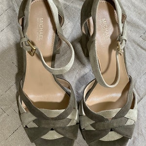 Pu&ograve; includere: Un paio di sandali con tacco in pelle scamosciata verde e beige con cinturini alla caviglia. Le sandali hanno un design incrociato sul davanti e il nome del marchio "MICHAEL MICHAEL KORS" &egrave; stampato sulla soletta.