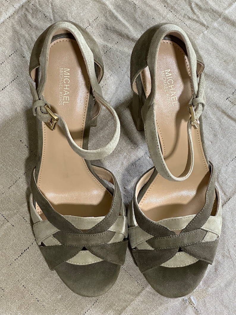 Pu&ograve; includere: Un paio di sandali con tacco in pelle scamosciata verde e beige con cinturini alla caviglia. Le sandali hanno un design incrociato sul davanti e il nome del marchio "MICHAEL MICHAEL KORS" &egrave; stampato sulla soletta.