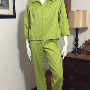 May include: A two-piece lime green outfit on a mannequin. The jacket has a collar, a zipper, and three-quarter sleeves. The pants are straight-legged. The outfit is made of a solid-colored fabric.