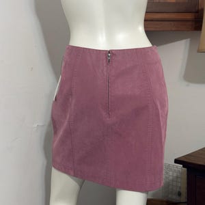 Op de afbeelding: Een stoffen mini-rok in de kleur roze met een ritssluiting aan de achterkant. De rok is gemaakt van een zacht, su&egrave;de-achtig materiaal en heeft verticale naden. De rok wordt op een mannequin getoond.