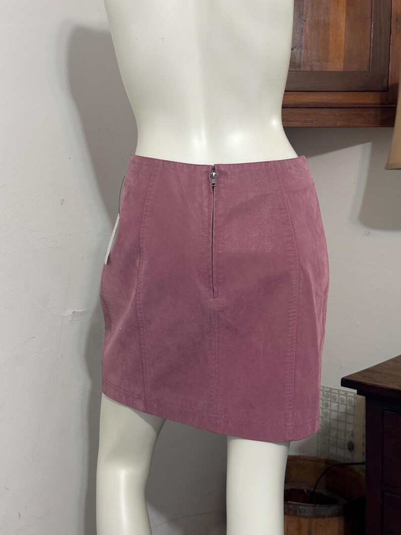 Op de afbeelding: Een stoffen mini-rok in de kleur roze met een ritssluiting aan de achterkant. De rok is gemaakt van een zacht, su&egrave;de-achtig materiaal en heeft verticale naden. De rok wordt op een mannequin getoond.