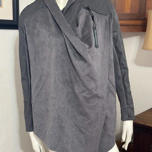 Pu&ograve; includere: Giacca grigia drappeggiata con un design asimmetrico unico. La giacca presenta un davanti drappeggiato, un dettaglio con cerniera e pannelli grigio scuro a contrasto sulle spalle e sulle maniche. Un'etichetta con il nome del marchio &egrave; attaccata.