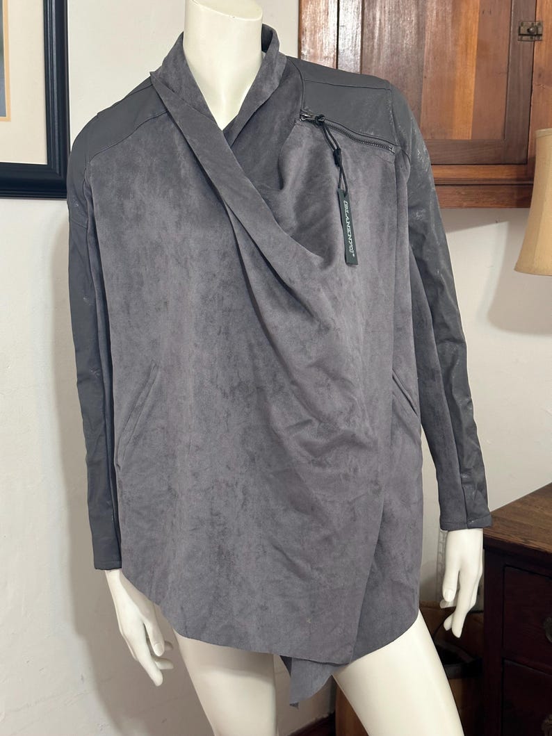 Pu&ograve; includere: Giacca grigia drappeggiata con un design asimmetrico unico. La giacca presenta un davanti drappeggiato, un dettaglio con cerniera e pannelli grigio scuro a contrasto sulle spalle e sulle maniche. Un'etichetta con il nome del marchio &egrave; attaccata.