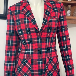 May include: A red, green, and white plaid blazer with two flap pockets. The blazer has a single button closure.