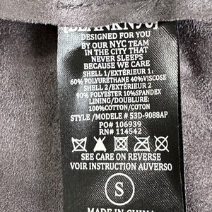 Pu&ograve; includere: Un'etichetta di abbigliamento nera con testo bianco, tra cui "DESIGNED FOR YOU BY OUR NYC TEAM" e istruzioni per la cura. L'etichetta elenca anche la composizione del tessuto e la taglia "S".
