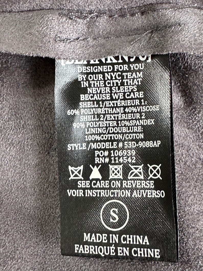 Pu&ograve; includere: Un'etichetta di abbigliamento nera con testo bianco, tra cui "DESIGNED FOR YOU BY OUR NYC TEAM" e istruzioni per la cura. L'etichetta elenca anche la composizione del tessuto e la taglia "S".