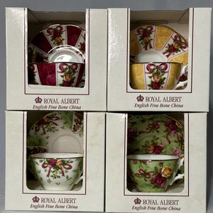 May include: Four boxed sets of Royal Albert English Fine Bone China teacups and saucers. Each set features a different floral and ribbon design in shades of red, yellow, and green. The teacups and saucers are displayed in individual boxes.
