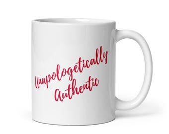 May include: A white ceramic mug with a curved handle. The mug features the words "Unapologetically Authentic" in a red, cursive font. The mug is designed for hot beverages.