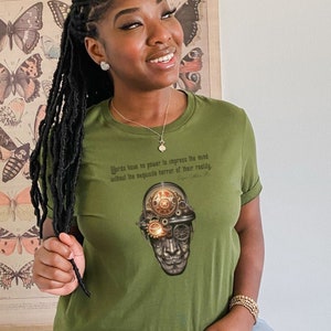 May include: A green t-shirt with a graphic of a steampunk-style skull with gears and a quote that reads "Works best on power to impress the mind without the requisite barrier of their readily"